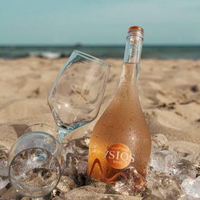 Bottle of rose with two glasses nestled in the sand 
